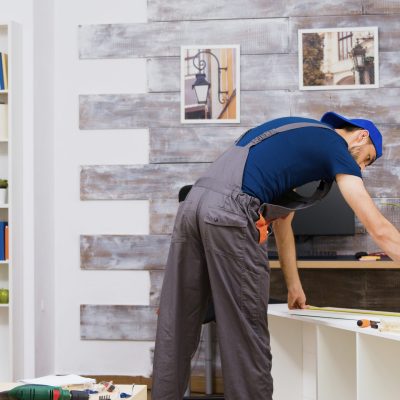 Furniture assembly worker standing reading instruction and using a tape measure. Worker tools.